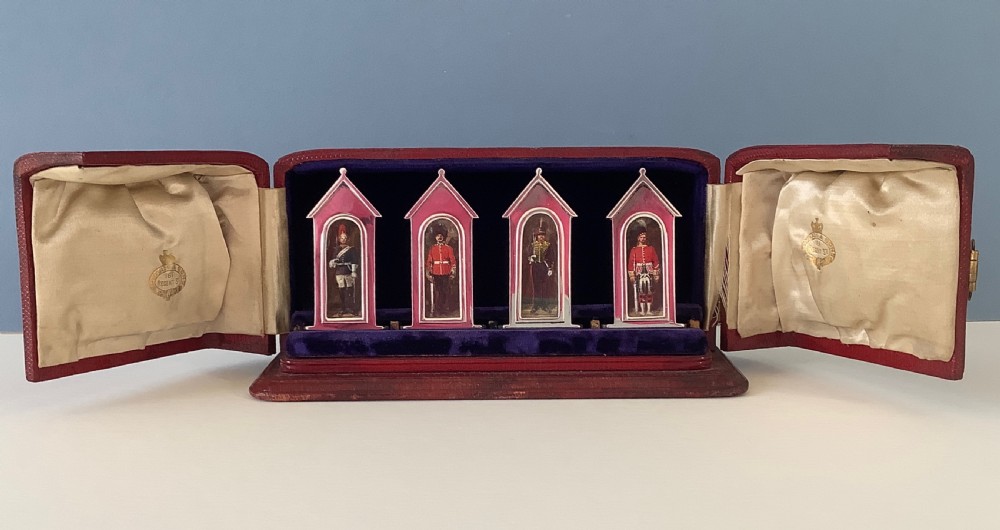 A set of four sterling silver and enamel sentry box menu holders featuring military guards inside a fitted red leather presentation case.