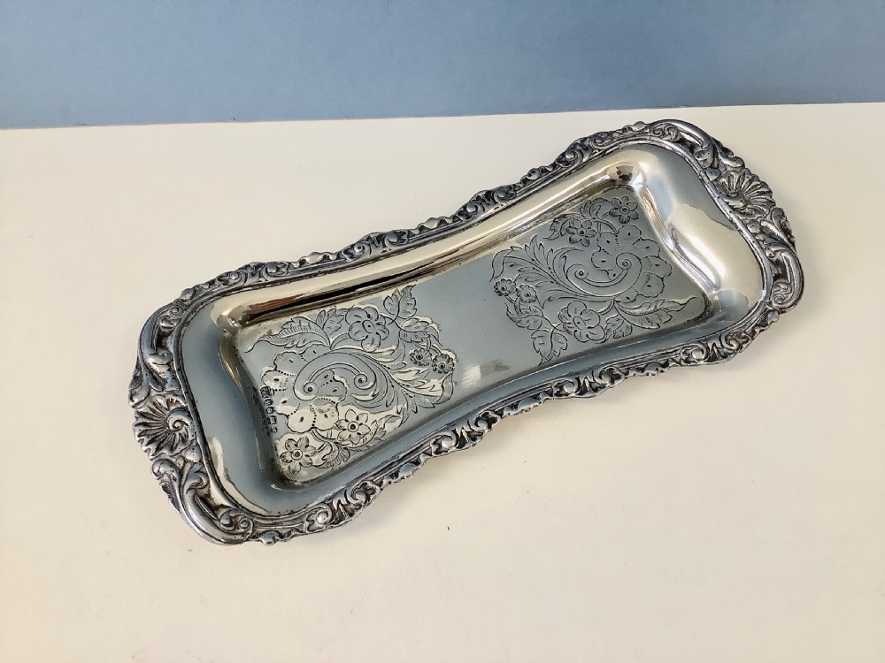An antique silver-plated scissor-style candle snuffer with a central box resting beside a matching oblong tray decorated with engraved floral motifs and scroll borders. View IV