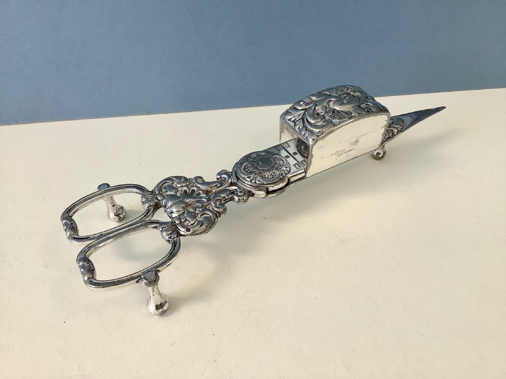 An antique silver-plated scissor-style candle snuffer with a central box resting beside a matching oblong tray decorated with engraved floral motifs and scroll borders. View VI