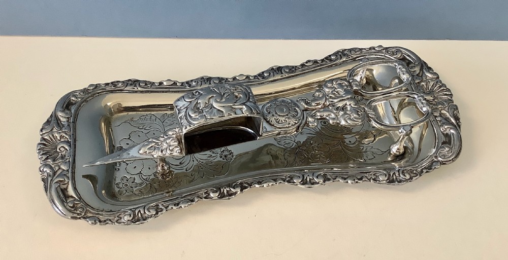 An antique silver-plated scissor-style candle snuffer with a central box resting beside a matching oblong tray decorated with engraved floral motifs and scroll borders. View VII