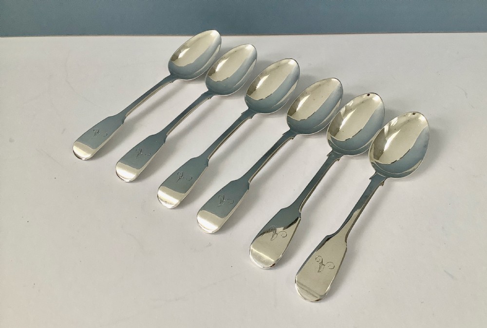 A set of six polished Victorian silver teaspoons featuring engraved monogrammed handles arranged neatly on a plain surface. View VII