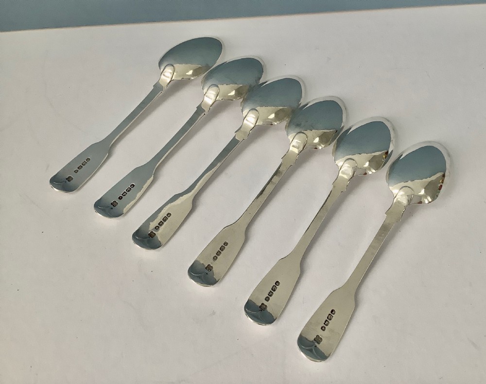 A set of six polished Victorian silver teaspoons featuring engraved monogrammed handles arranged neatly on a plain surface. View II