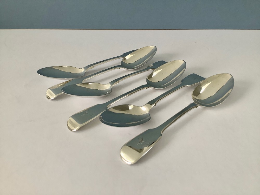 A set of six polished Victorian silver teaspoons featuring engraved monogrammed handles arranged neatly on a plain surface. View VI