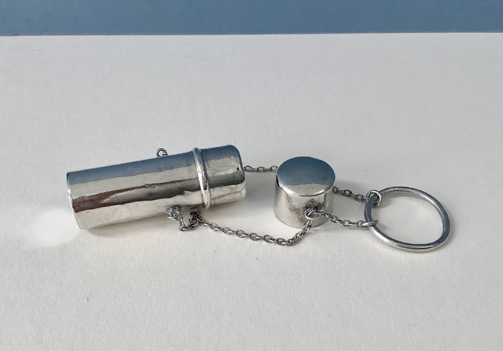 An antique Edwardian cylindrical sterling silver needle case featuring stamped silver hallmarks, attached to fine link chains and a suspension ring. View IV