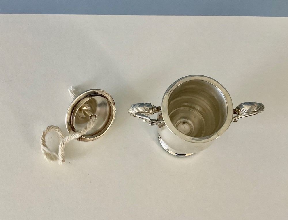 An antique urn-shaped sterling silver table lighter featuring twin scroll handles, a domed lid, and a protruding cotton wick. View V