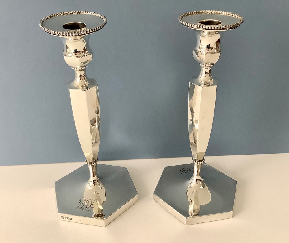 A pair of polished silver candlesticks with hexagonal bases, faceted columns, beaded rims, and engraved monograms.