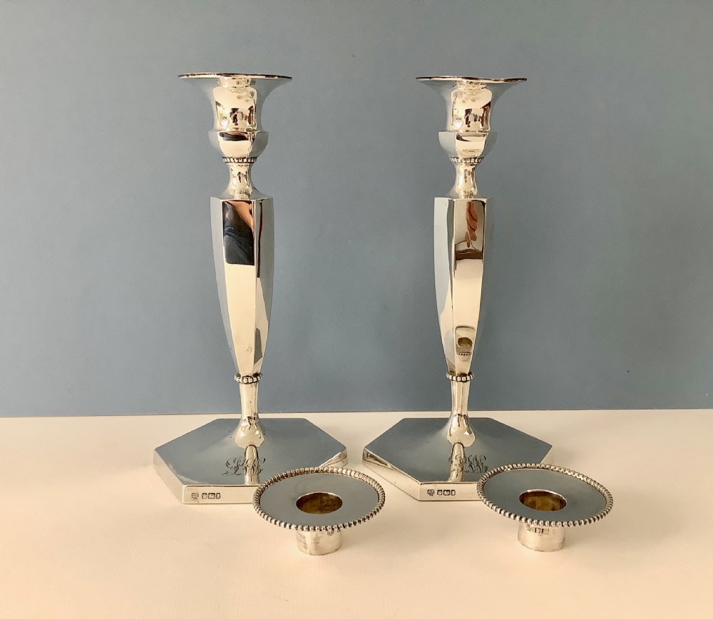 A pair of polished silver candlesticks with hexagonal bases, faceted columns, beaded rims, and engraved monograms. View VI