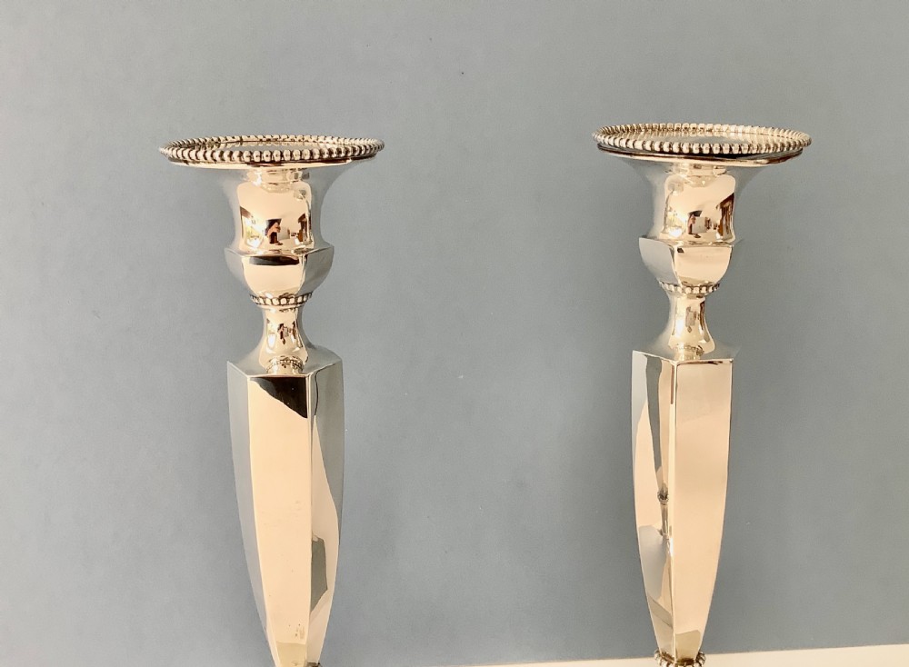 A pair of polished silver candlesticks with hexagonal bases, faceted columns, beaded rims, and engraved monograms. View VII