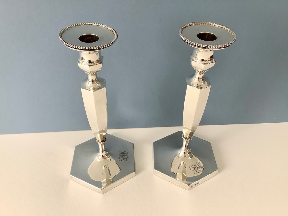 A pair of polished silver candlesticks with hexagonal bases, faceted columns, beaded rims, and engraved monograms. View IX