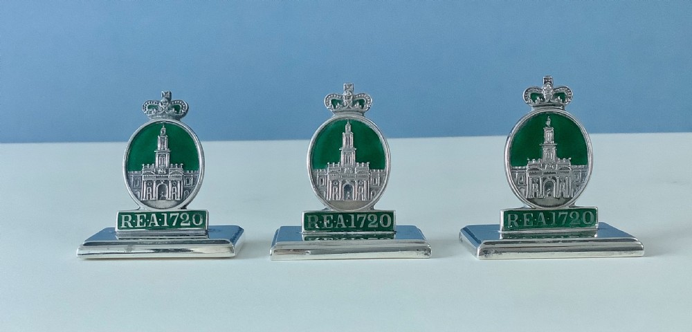 A set of three antique solid silver and green enamel menu holders featuring a crowned crest and rectangular bases.