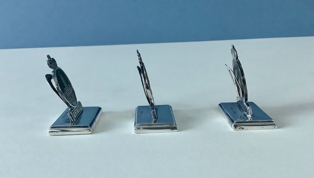 A set of three antique solid silver and green enamel menu holders featuring a crowned crest and rectangular bases. View VI