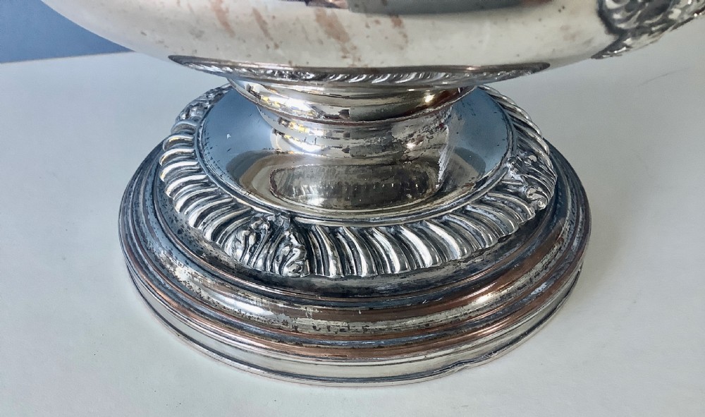 A Georgian silver-plated urn-shaped wine cooler featuring gadrooned borders, a pedestal base, and twin decorative side handles. View V