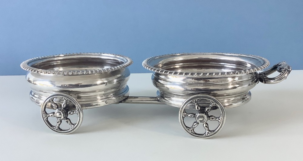 A Georgian Old Sheffield Plate double wine coaster trolley featuring two gadrooned circular holders joined on a wheeled frame with a small end handle.