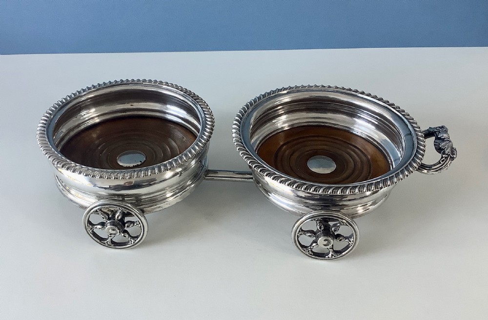 A Georgian Old Sheffield Plate double wine coaster trolley featuring two gadrooned circular holders joined on a wheeled frame with a small end handle. View II