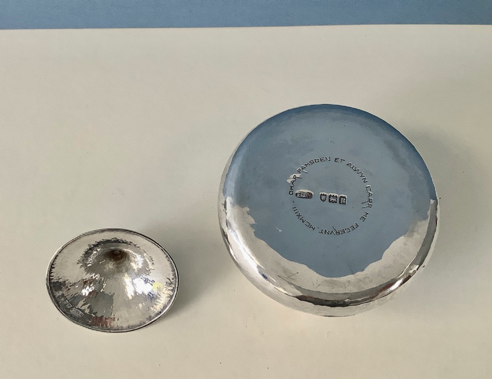A hand-hammered sterling silver lidded box featuring a conical cover, a decorative finial, and an engraved heraldic crest. View VI