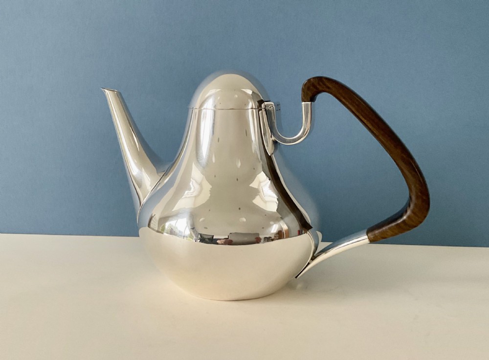 A polished silver Georg Jensen coffee pot featuring a bulbous teardrop body, seamless tapered spout, and a dark carved wooden handle.
