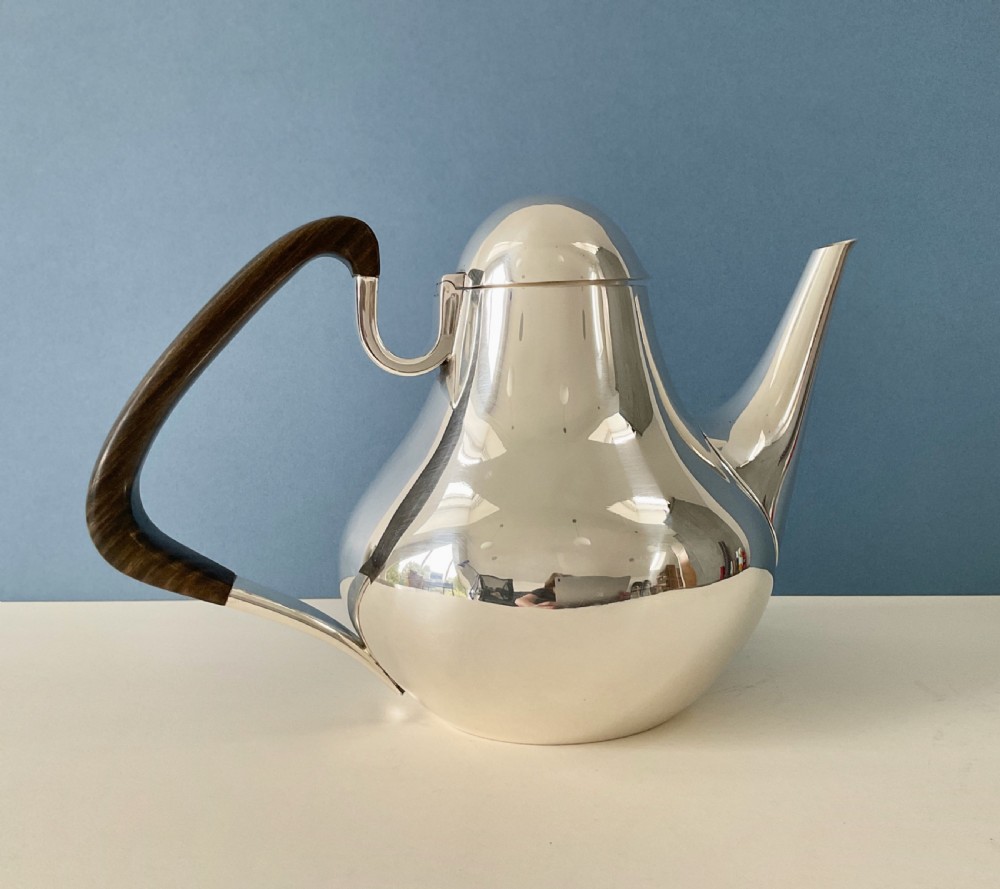 A polished silver Georg Jensen coffee pot featuring a bulbous teardrop body, seamless tapered spout, and a dark carved wooden handle. View III