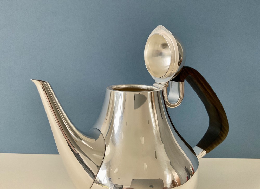 A polished silver Georg Jensen coffee pot featuring a bulbous teardrop body, seamless tapered spout, and a dark carved wooden handle. View VI