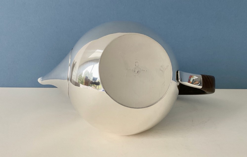 A polished silver Georg Jensen coffee pot featuring a bulbous teardrop body, seamless tapered spout, and a dark carved wooden handle. View VII