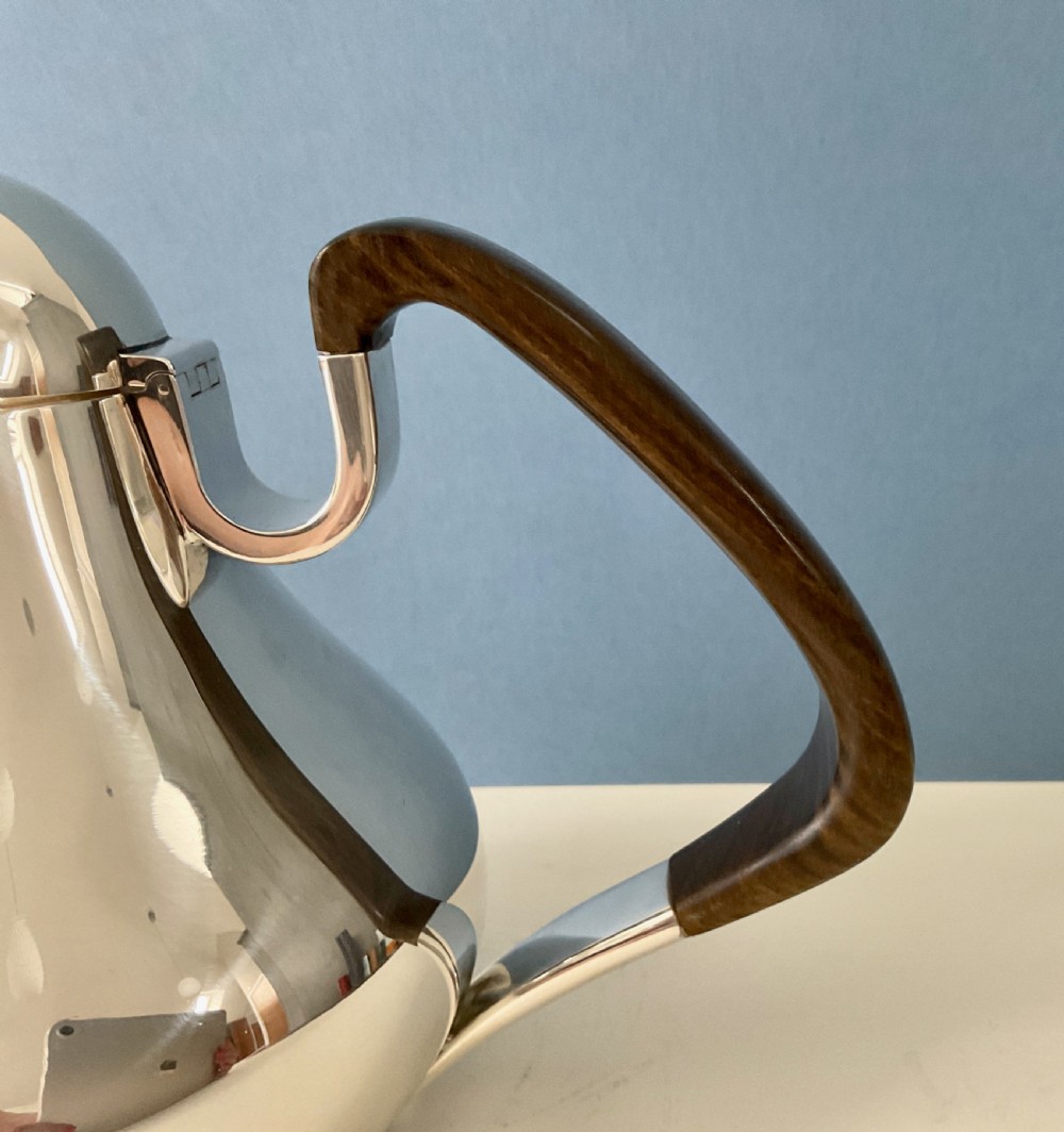A polished silver Georg Jensen coffee pot featuring a bulbous teardrop body, seamless tapered spout, and a dark carved wooden handle. View IX