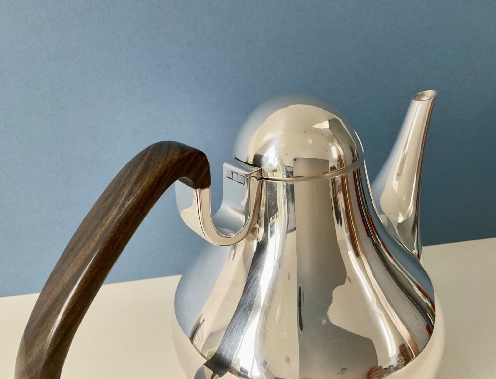 A polished silver Georg Jensen coffee pot featuring a bulbous teardrop body, seamless tapered spout, and a dark carved wooden handle. View X