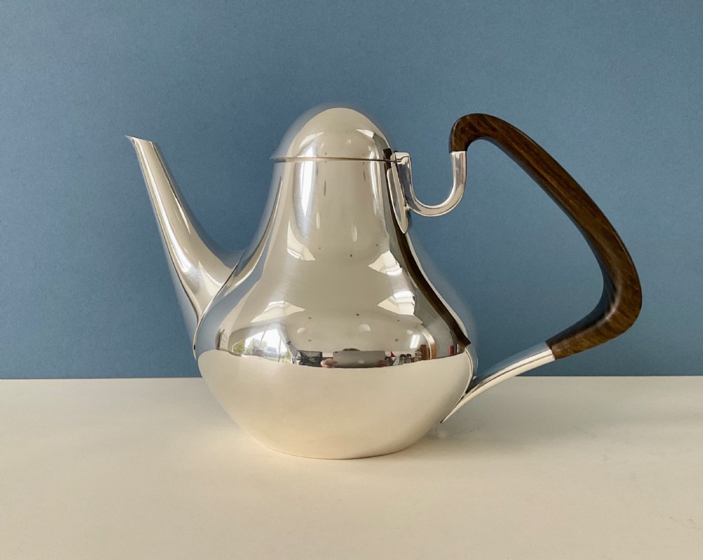 A polished silver Georg Jensen coffee pot featuring a bulbous teardrop body, seamless tapered spout, and a dark carved wooden handle. View XI