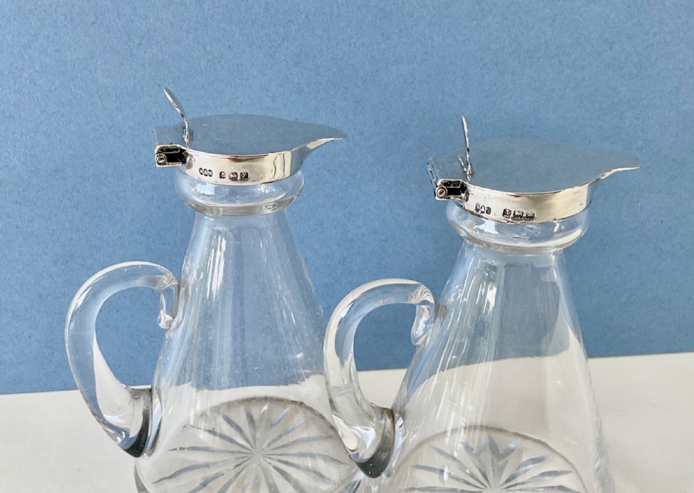 A pair of conical clear glass whisky noggins featuring silver hinged caps, side handles, star-cut bases, and silver Whisky tags. View II