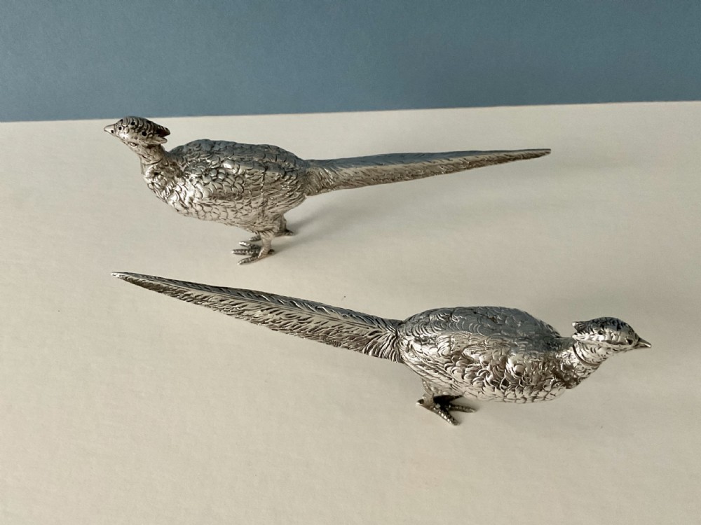 A pair of detailed solid silver pepper shakers crafted in the form of standing pheasants with long tail feathers.