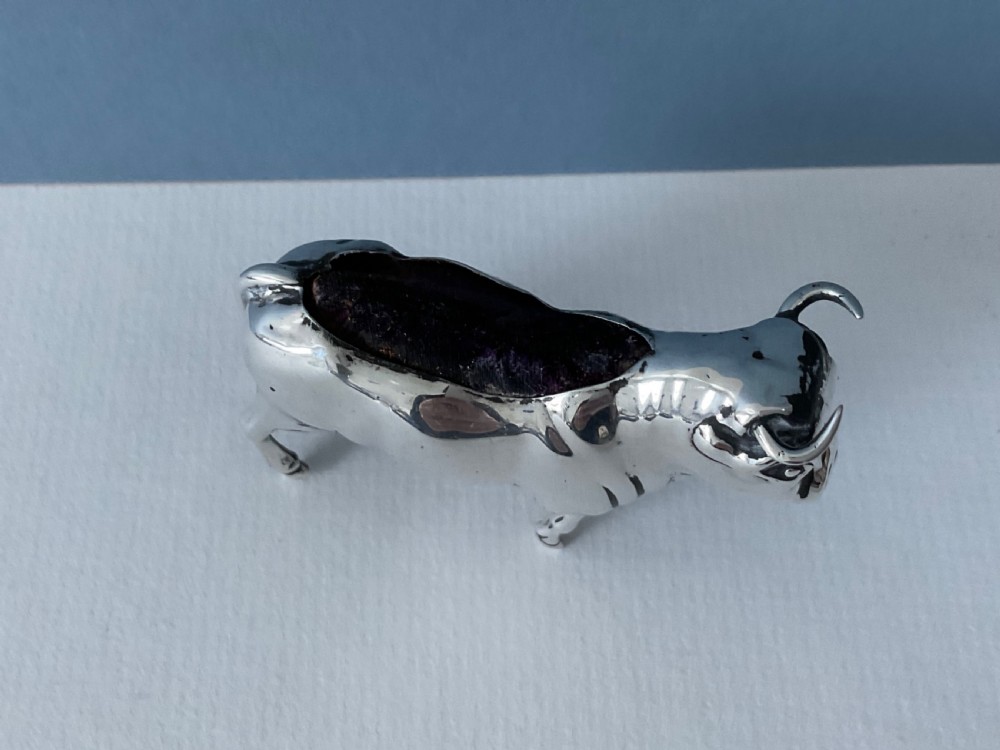 A small cast silver pin cushion shaped like a standing bull with a dark velvet insert fitted into its back. View V