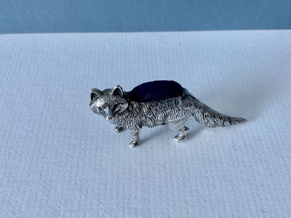 A cast silver pin cushion shaped as a standing fox with detailed fur texture and a dark blue velvet cushion fitted on its back.