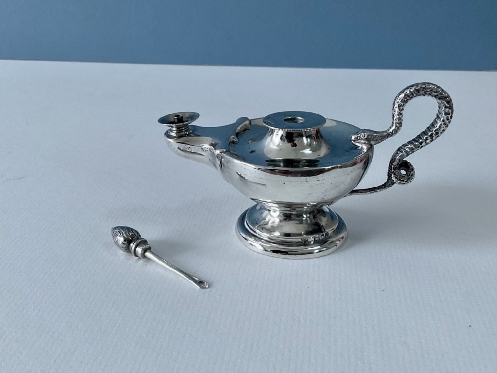A polished silver table lighter modelled in the shape of an ancient oil lamp with a coiled serpent handle and a pedestal base. View II