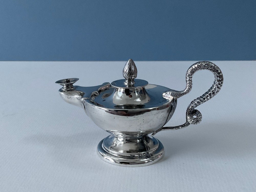 A polished silver table lighter modelled in the shape of an ancient oil lamp with a coiled serpent handle and a pedestal base. View V