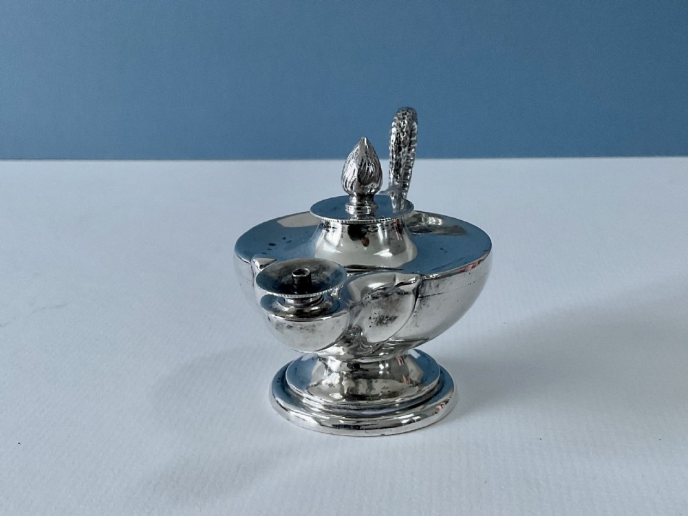 A polished silver table lighter modelled in the shape of an ancient oil lamp with a coiled serpent handle and a pedestal base. View VII