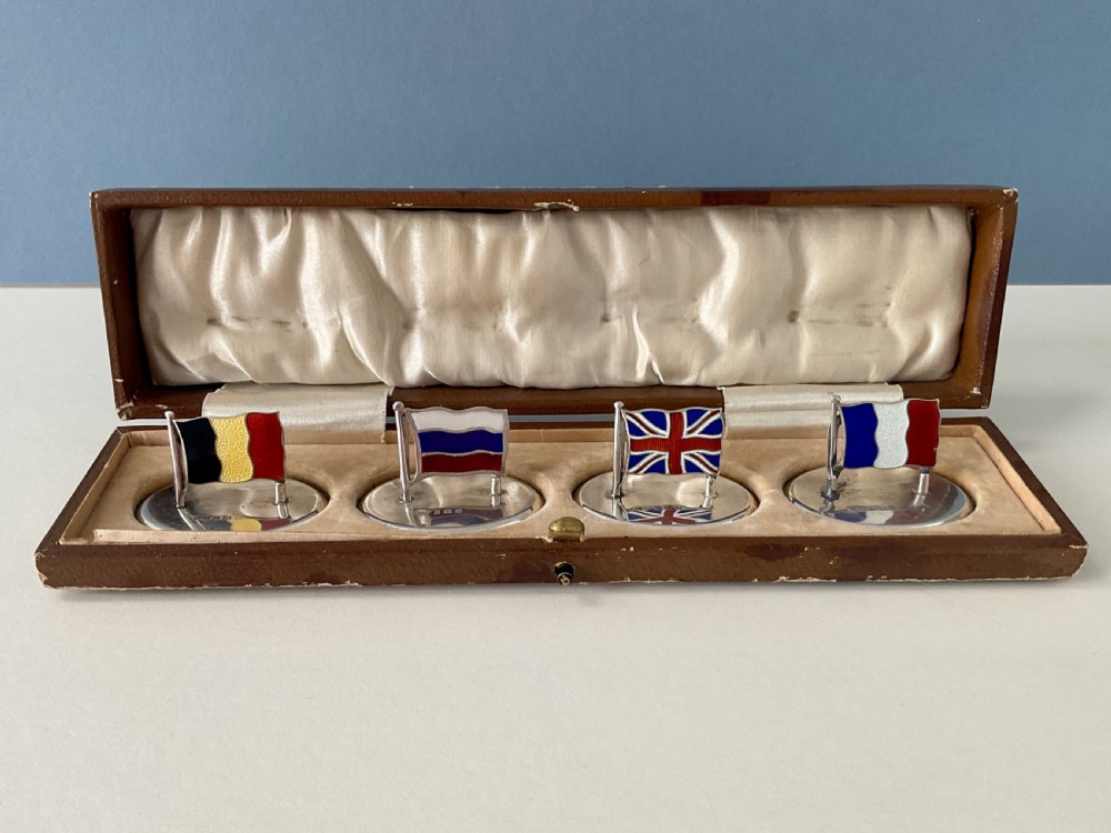 A set of four Edwardian silver and colourful enamel flag menu holders housed within a fitted brown presentation box.