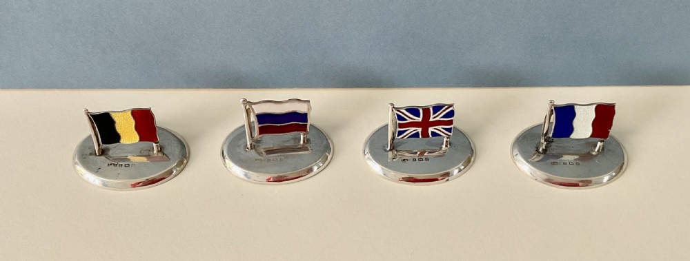 A set of four Edwardian silver and colourful enamel flag menu holders housed within a fitted brown presentation box. View X