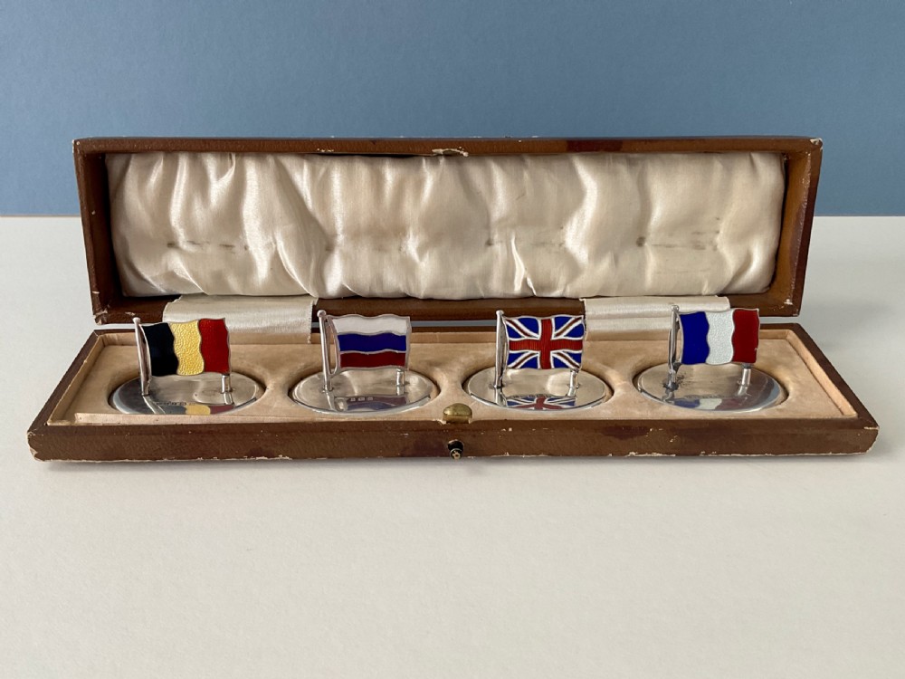 A set of four Edwardian silver and colourful enamel flag menu holders housed within a fitted brown presentation box. View XII