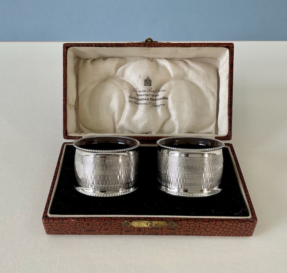 A pair of circular sterling silver napkin rings featuring engine-turned geometric patterns, beaded edges, and dark interior linings. View II