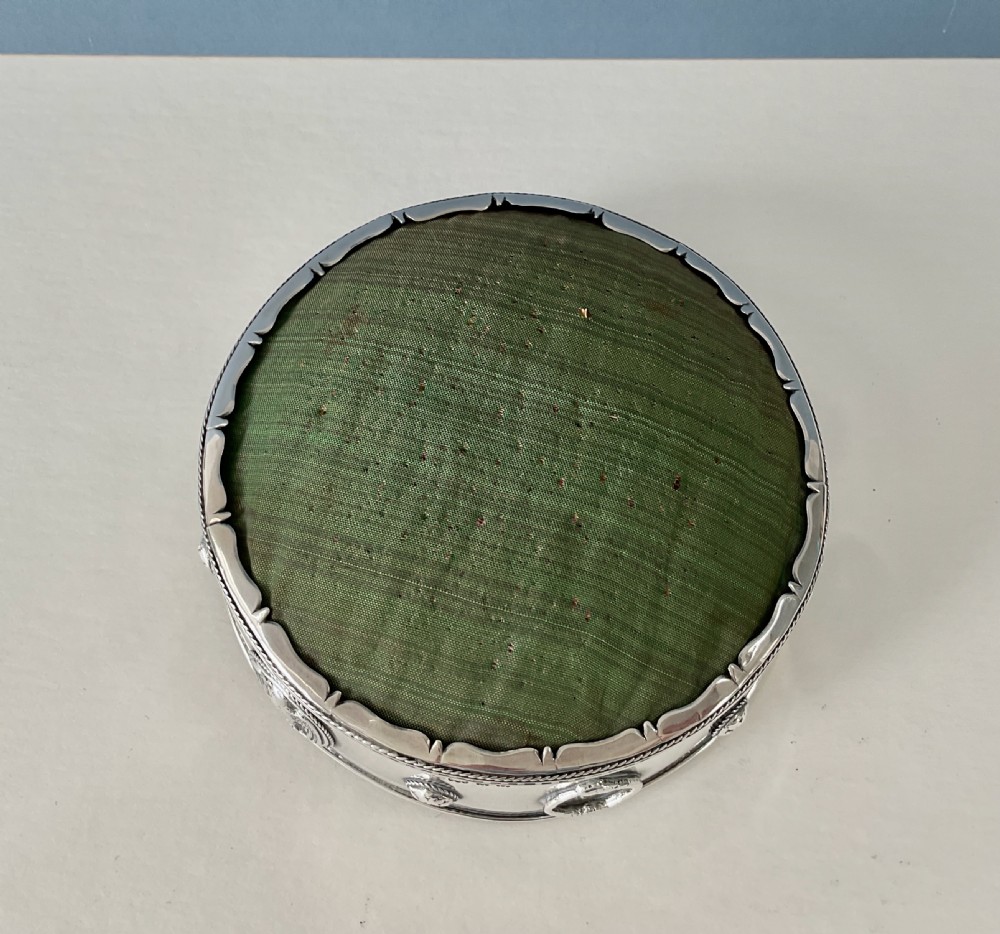 A circular Arts and Crafts silver pin cushion stand with embossed eagle medallions and a raised green woven fabric top. View III
