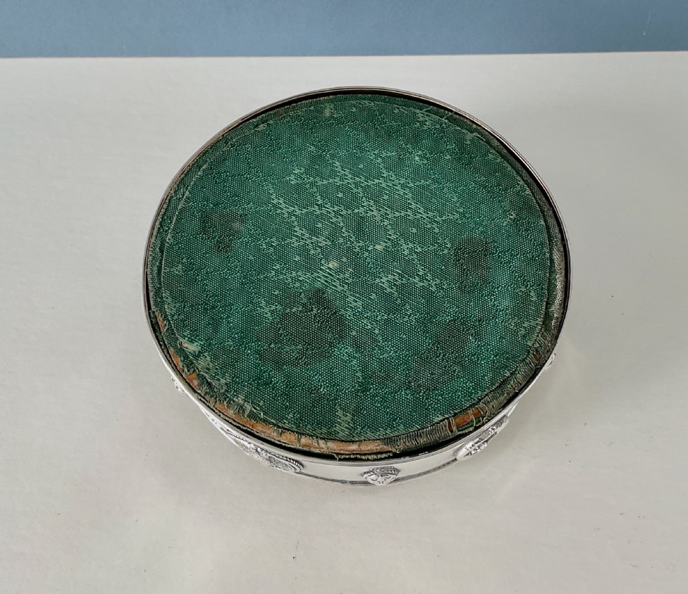 A circular Arts and Crafts silver pin cushion stand with embossed eagle medallions and a raised green woven fabric top. View VI