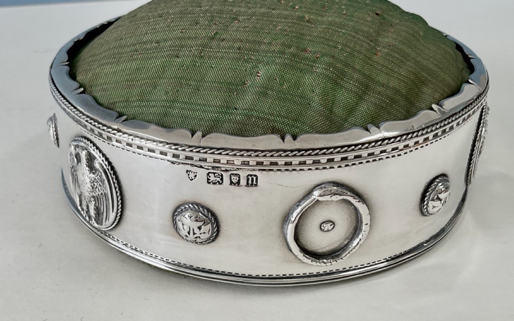 A circular Arts and Crafts silver pin cushion stand with embossed eagle medallions and a raised green woven fabric top. View VII
