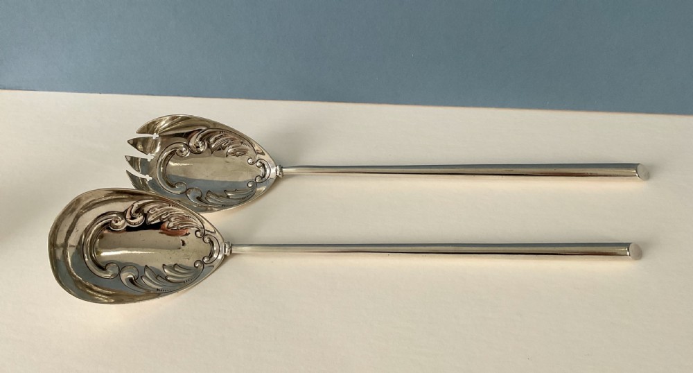 A pair of antique silver salad servers with long slender handles and embossed scrollwork on the spoon and fork bowls. View II