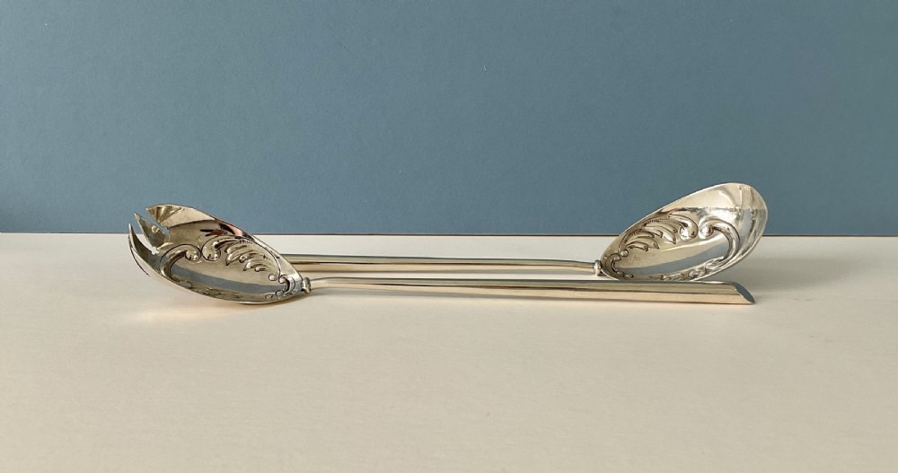 A pair of antique silver salad servers with long slender handles and embossed scrollwork on the spoon and fork bowls. View III