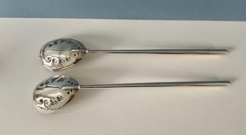 A pair of antique silver salad servers with long slender handles and embossed scrollwork on the spoon and fork bowls. View V