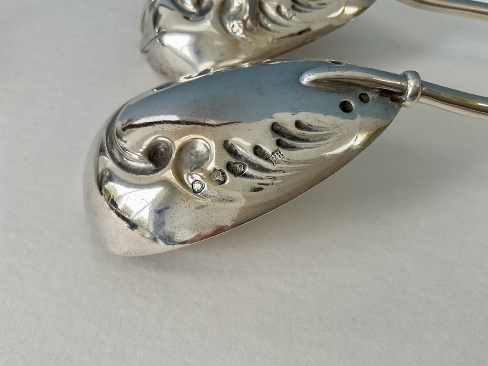 A pair of antique silver salad servers with long slender handles and embossed scrollwork on the spoon and fork bowls. View VII