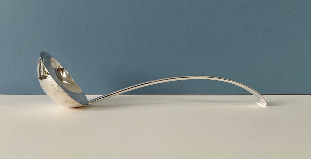 A silver-plated soup ladle featuring a deep hemispherical bowl and a long curved handle resting horizontally on a light surface.