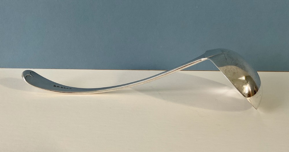 A silver-plated soup ladle featuring a deep hemispherical bowl and a long curved handle resting horizontally on a light surface. View II