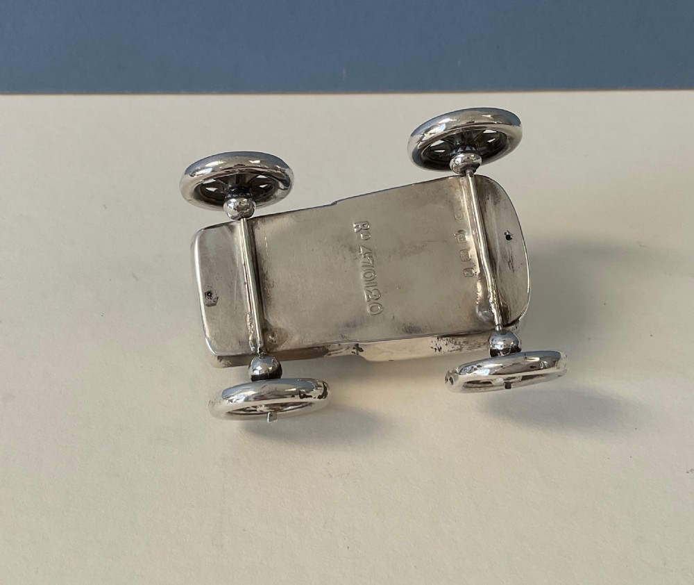 An antique silver pin cushion cast in the shape of an early motor car featuring spoked wheels and a fabric cushion fitted into the seat. View V