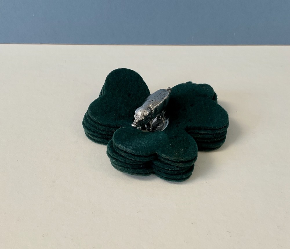 An antique silver pig finial mounted on stacked dark green clover-shaped felt pads. View V