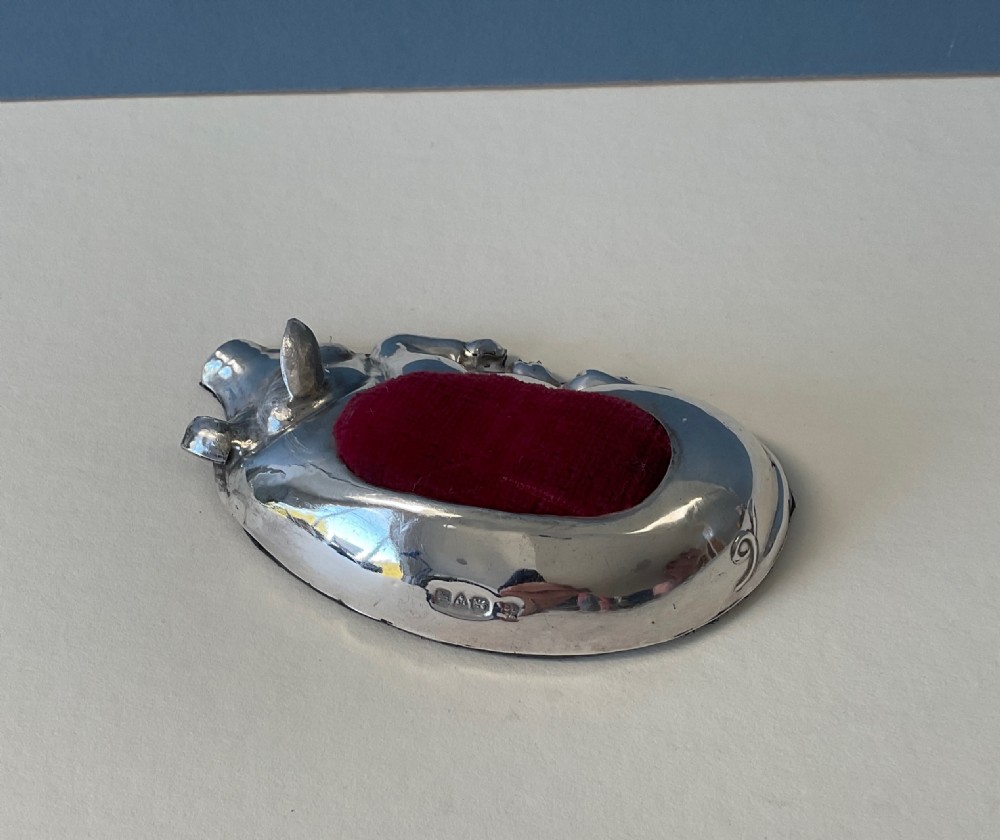 An antique silver pin cushion cast in the form of a recumbent pig with a red velvet cushion insert in its back. View II