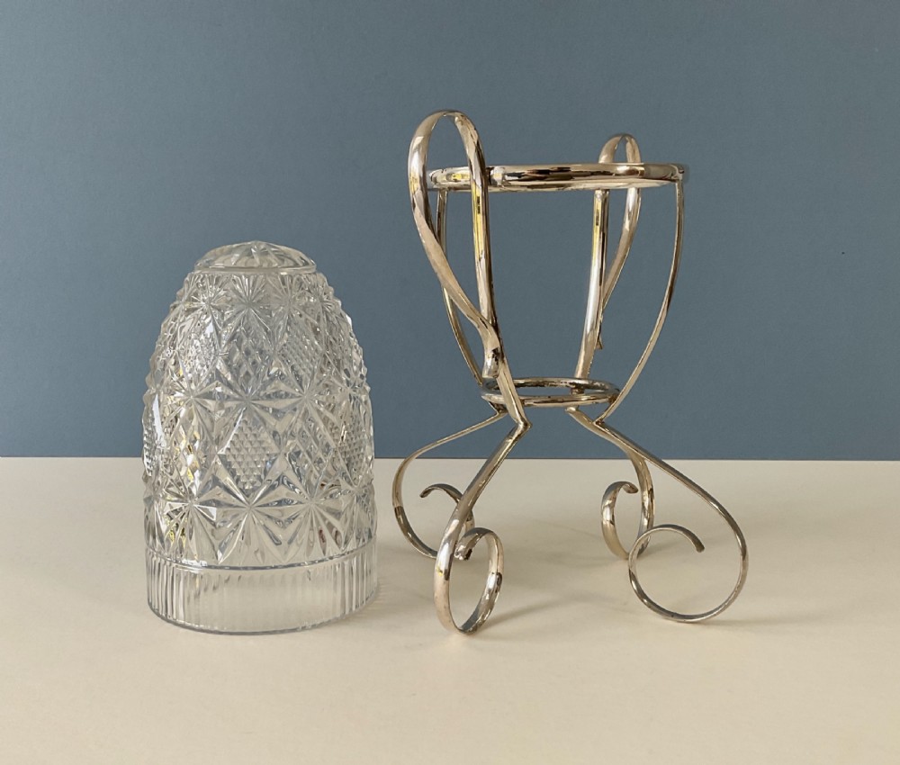A clear cut-glass cylindrical vase featuring diamond motifs resting inside a silver-plated wire frame with scrolled handles and feet. View IV